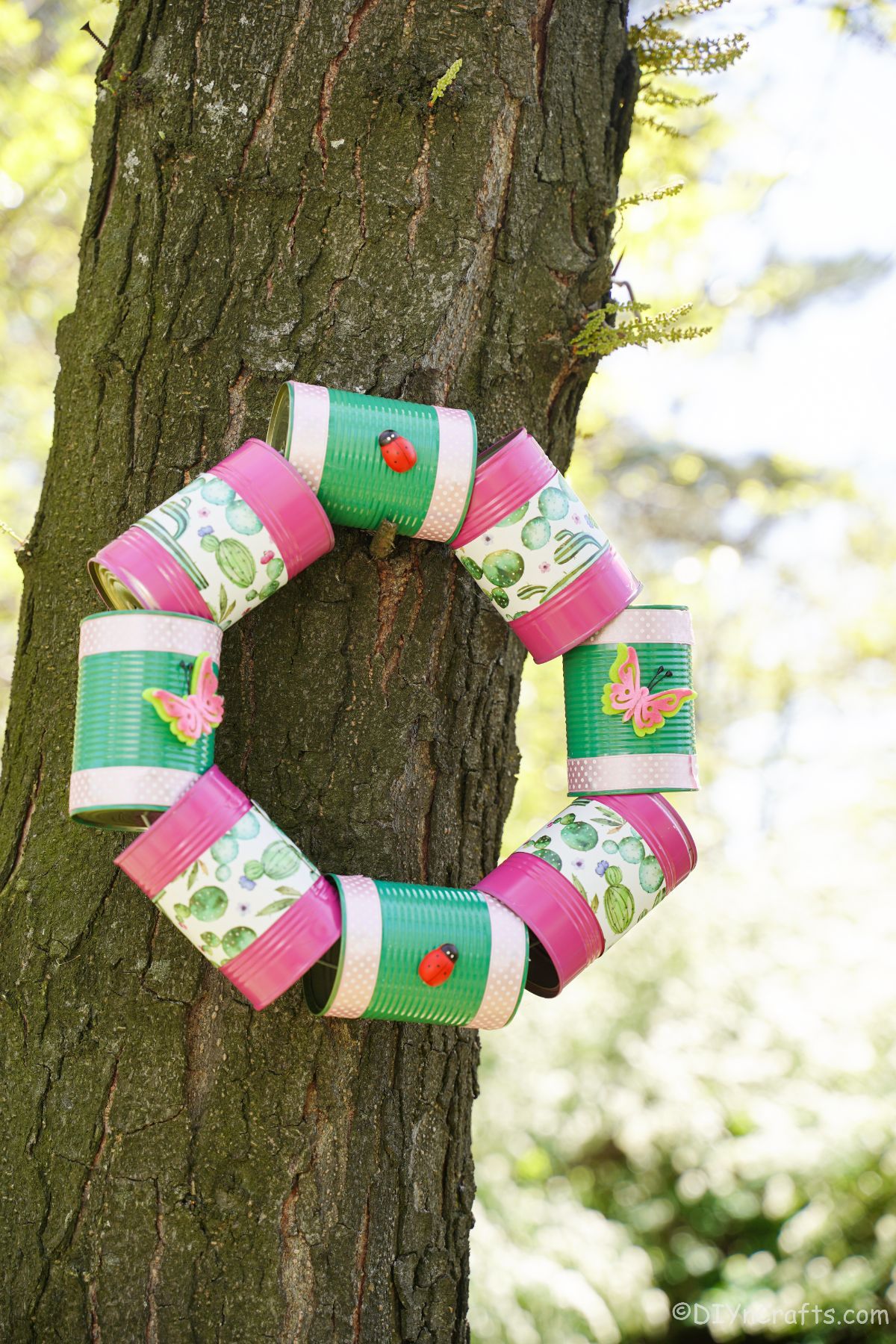 pink and green tin can wreath hanging on tree trunk
