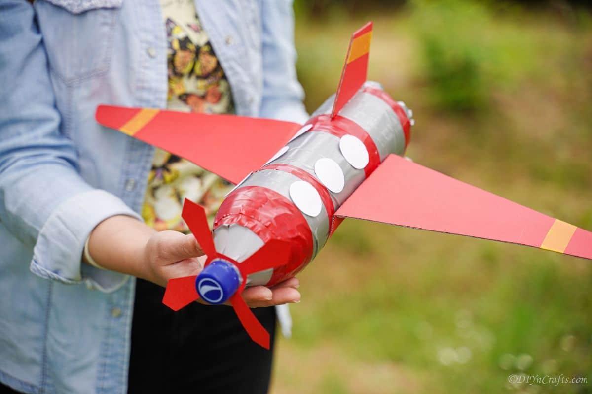 woman in blue holding toy airplane made of plastic bottles