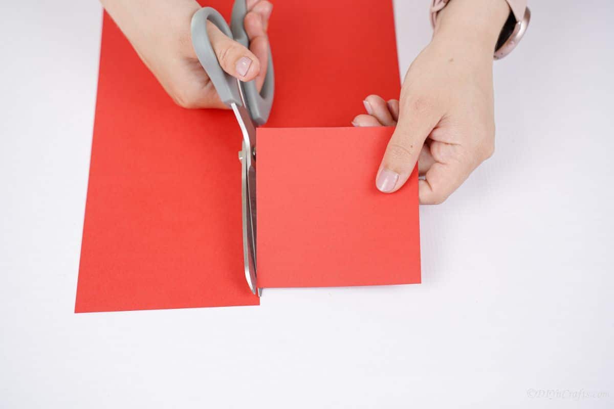 gray scissors being used to cut square of red paper