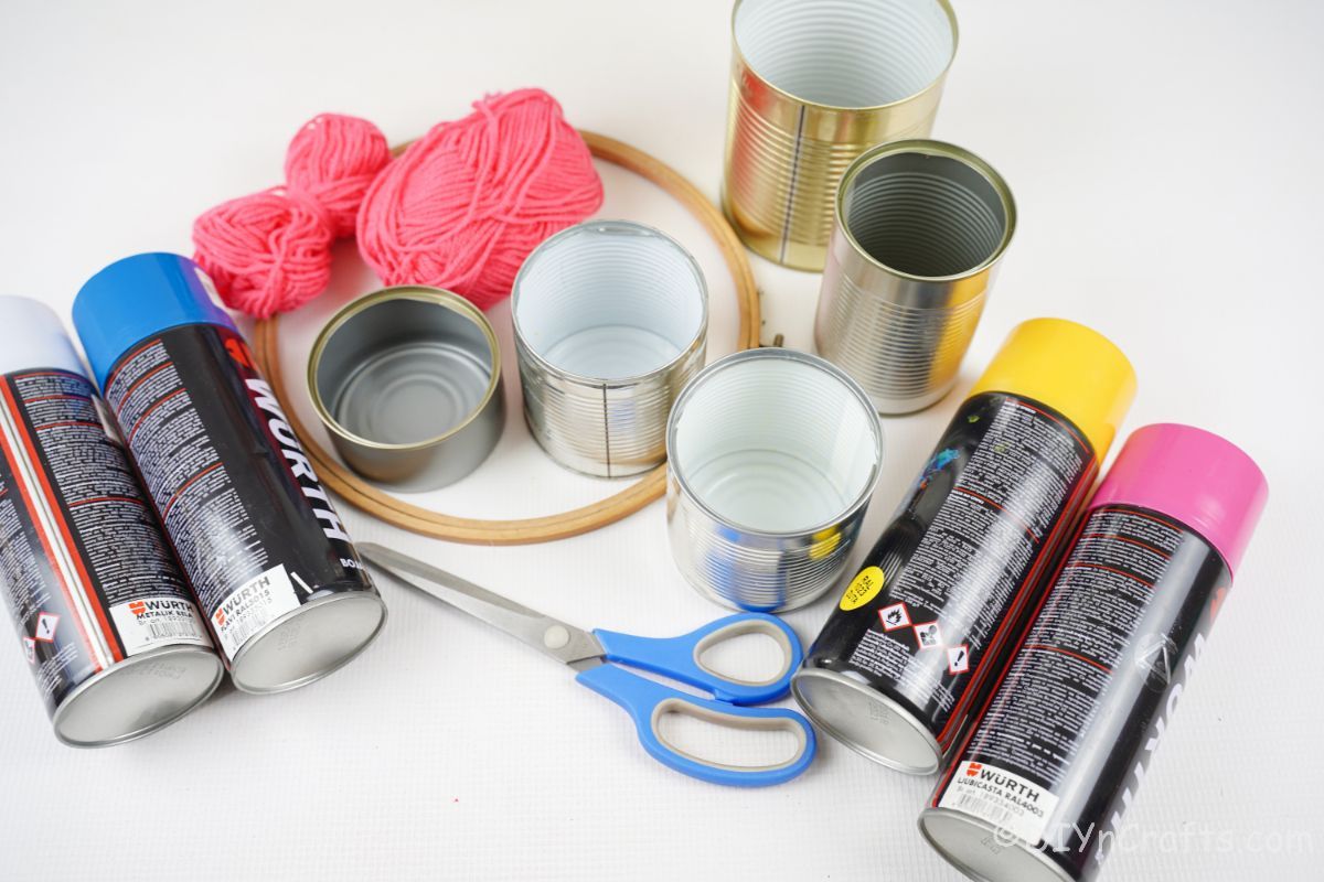 several cans of spray paint tin cans and embroidery hoop with yarn on white table