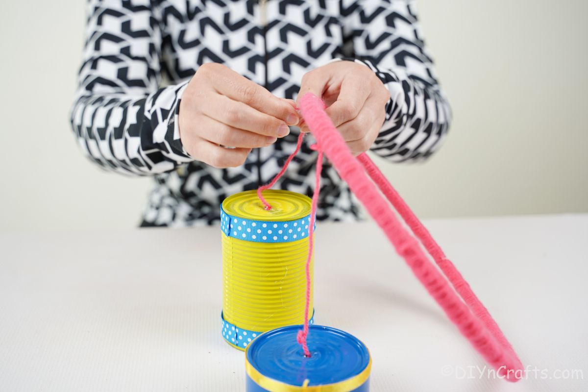 hand tying tin cans to pink wrapped embroidery loop