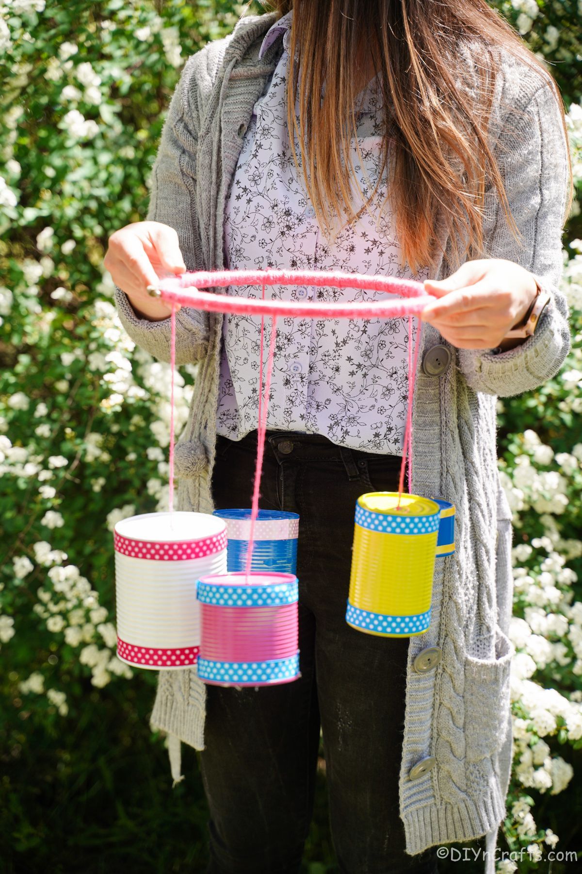 woman holding colorful windchime in front of white shrubs