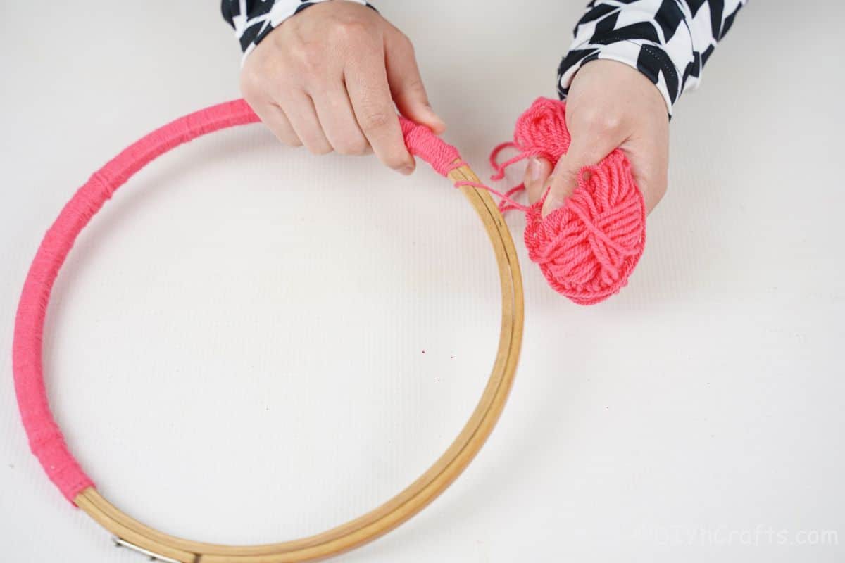 hand wrapping pink yarn around embroidery hoop