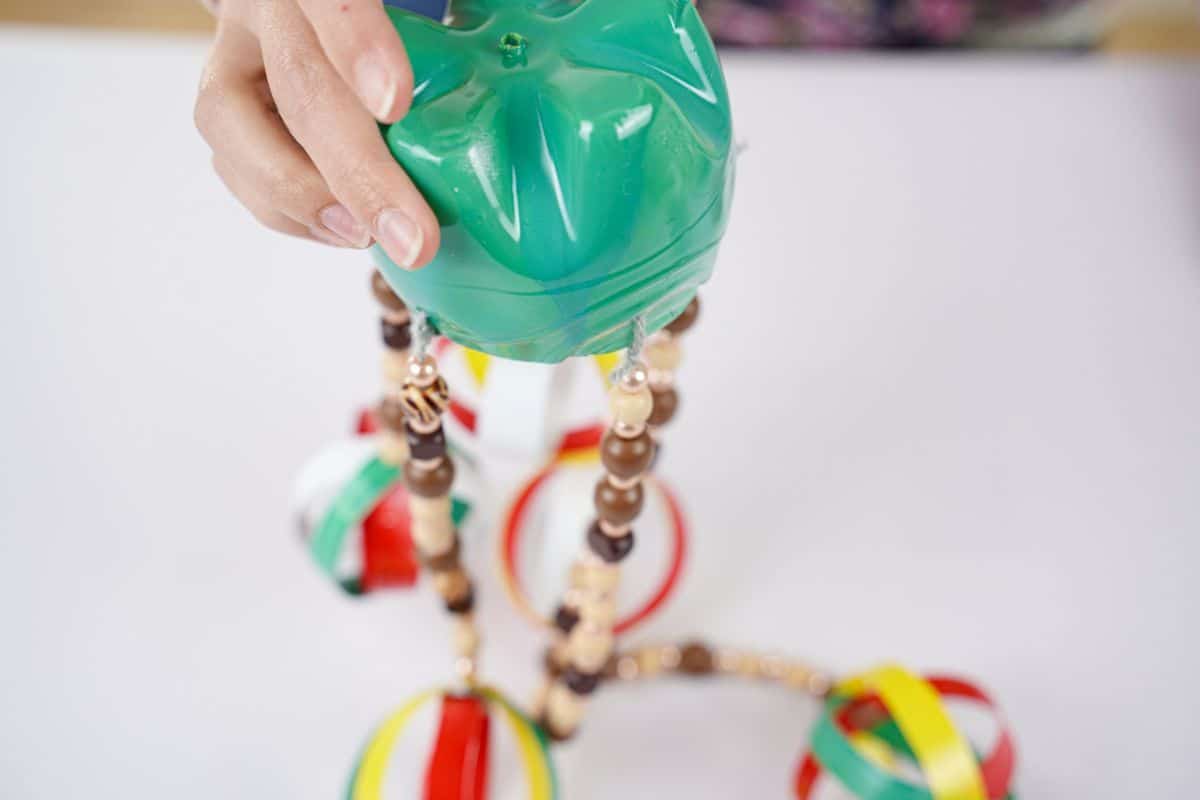 hand holding green bottle with beads hanging on white table