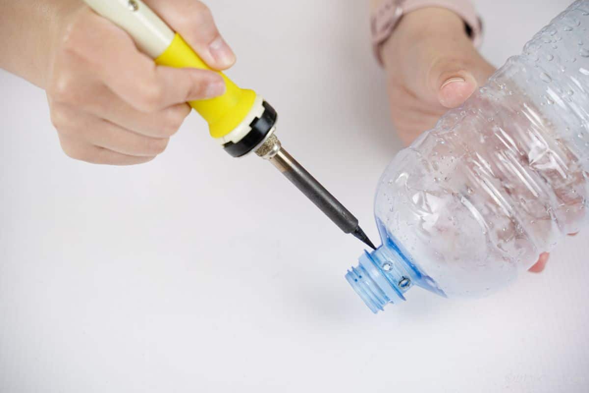 hand holding soldering iron on side of bottle to make holes