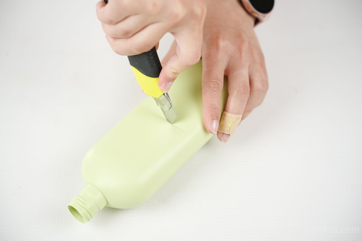 hand using craft knife to cut green bottle