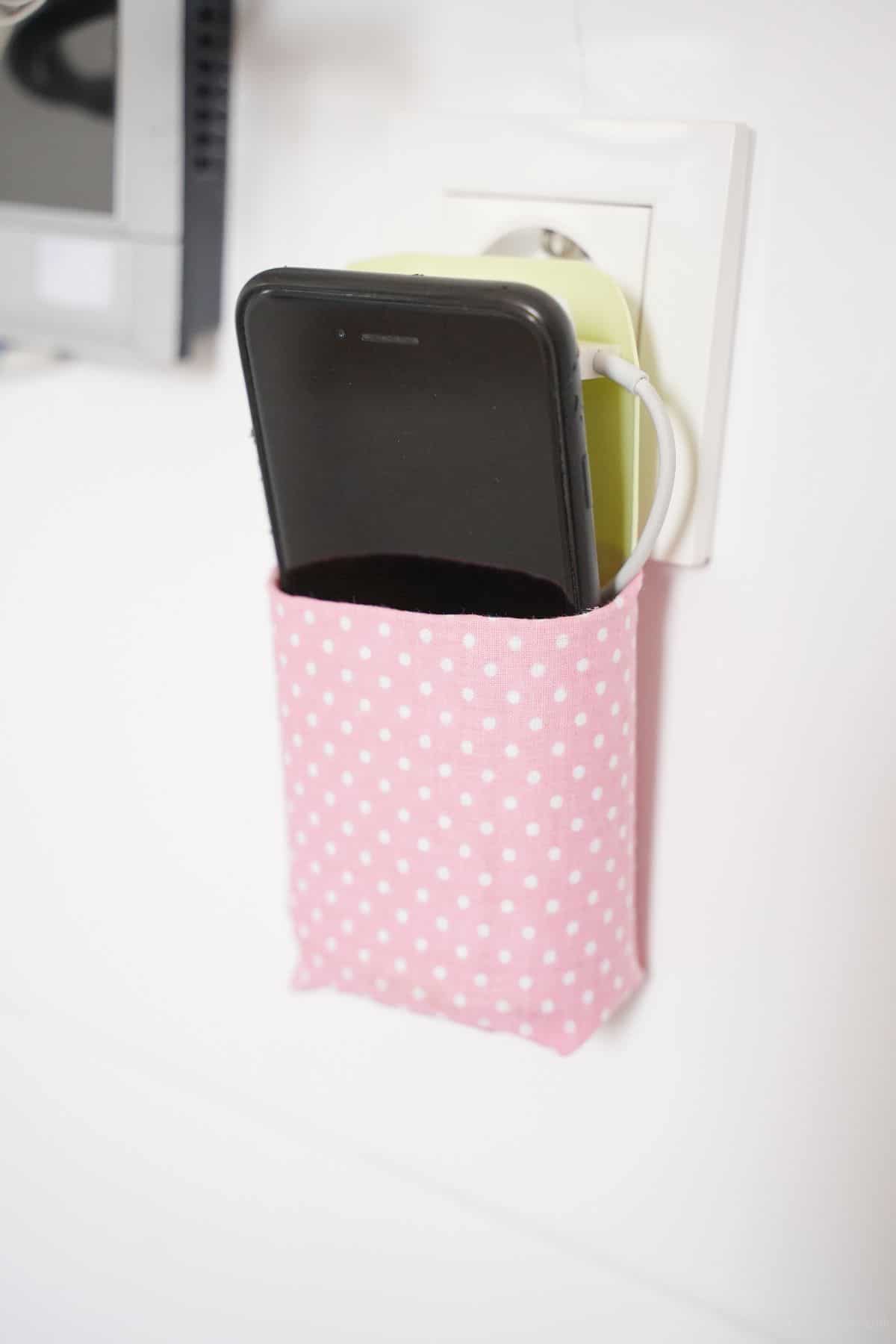 white and pink holder for cellphone hanging on white outlet