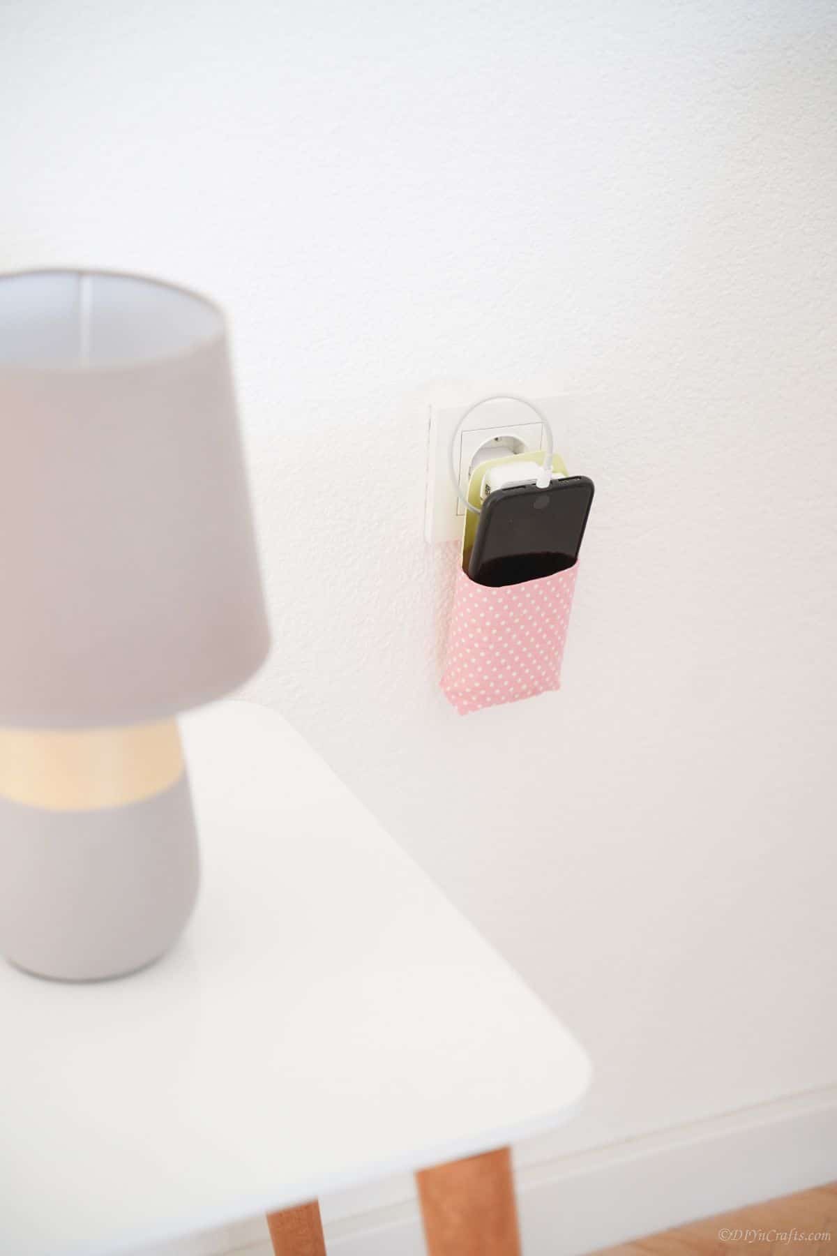 white table with gray lamp next to pink cellphone holder on wall