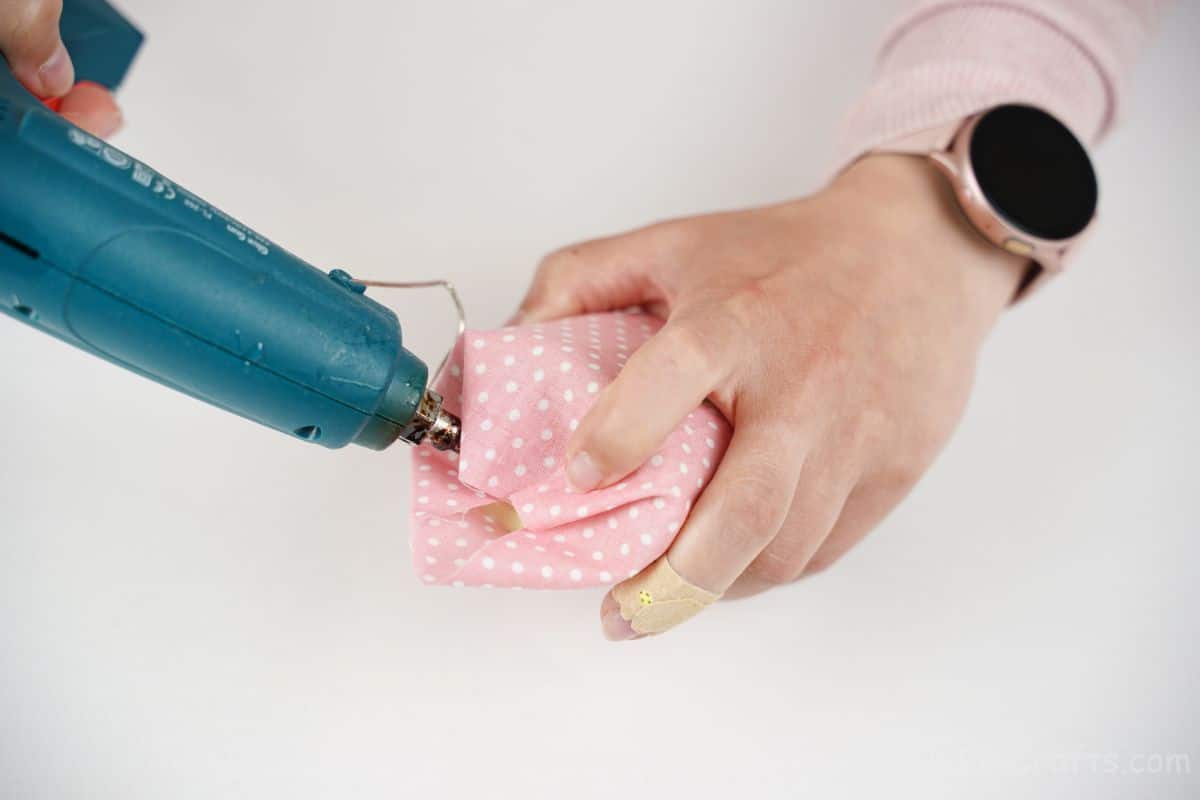 woman holding glue gun and pink fabric on bottle