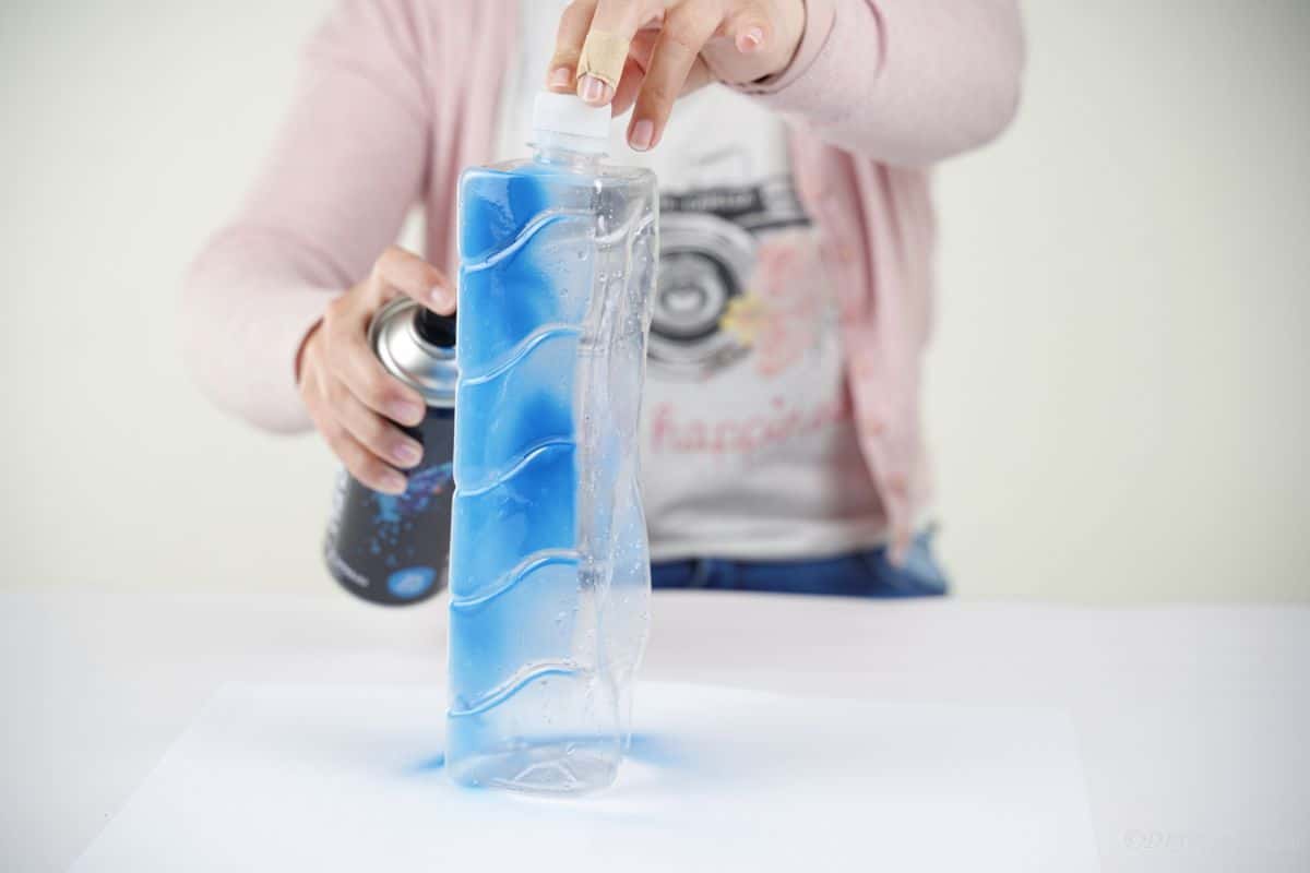 hand holding clear bottle to spray it blue