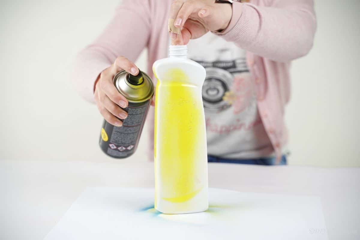 hand holding white bottle while it is being sprayed yellow