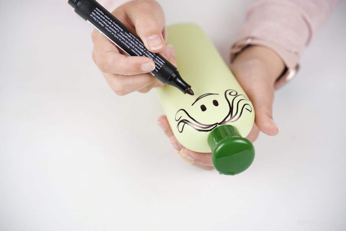 black marker being used to draw a face on green bottle