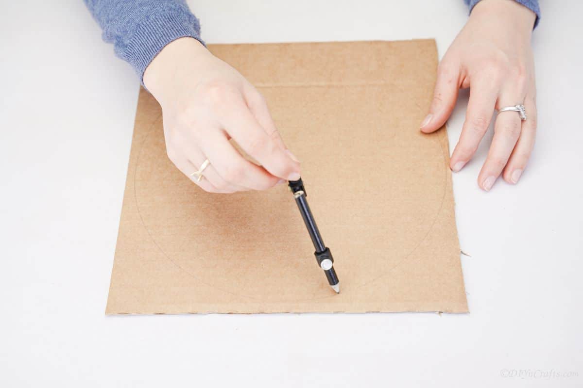 hand holding pencil to draw circle on cardboard