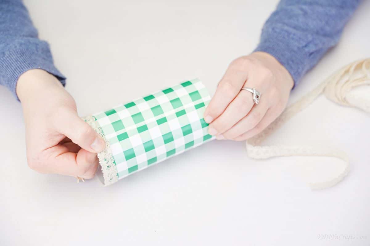 hands wrapping lace on ends of bottle wrappe din green and white paper