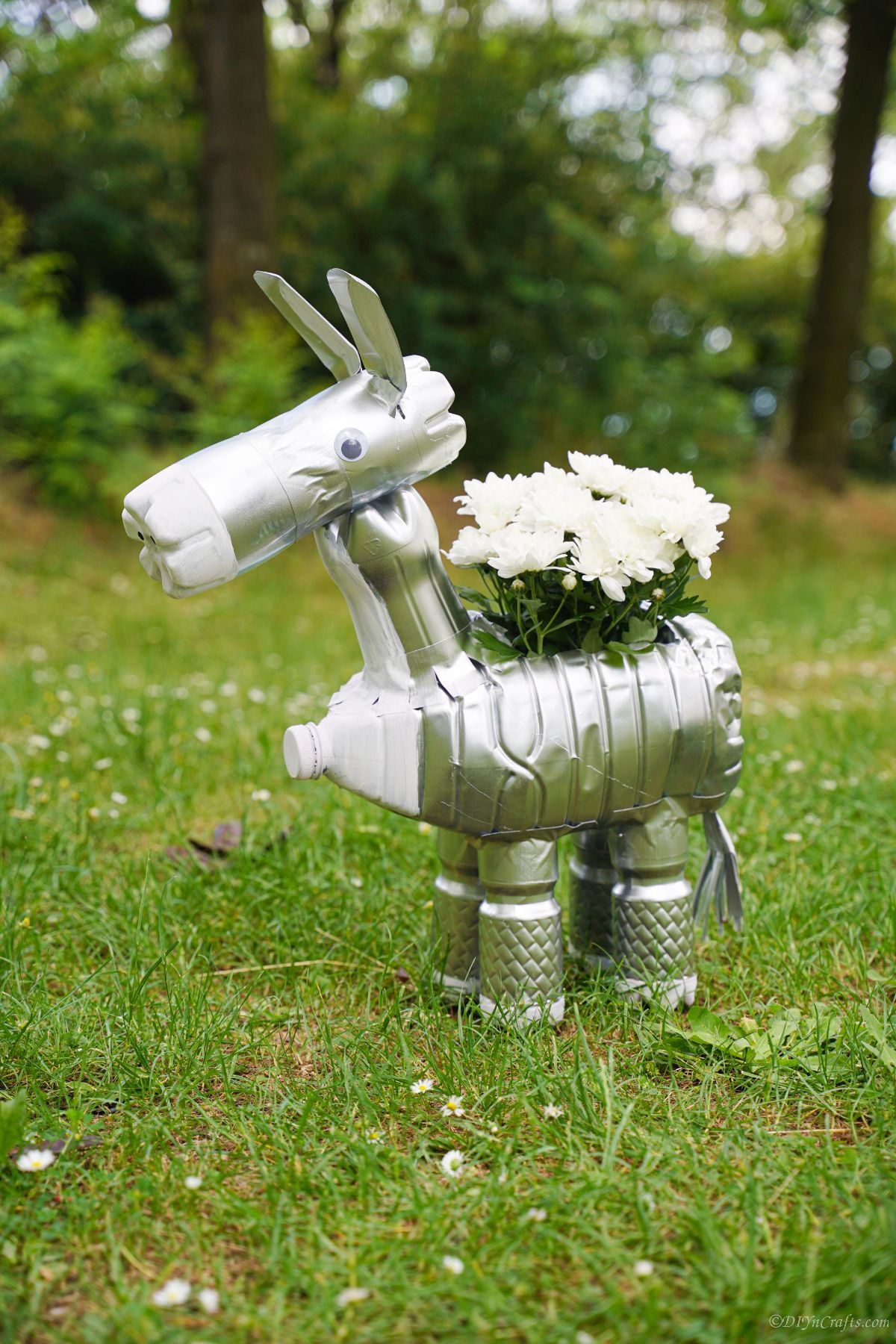 bottle donkey with silver spray paint outside in front of trees