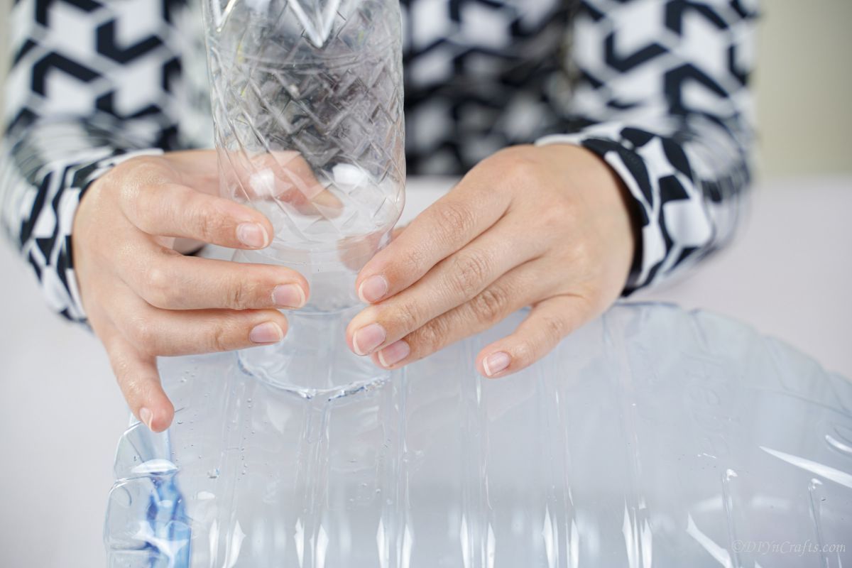 hand holding plastic bottle on top of larger water bottle