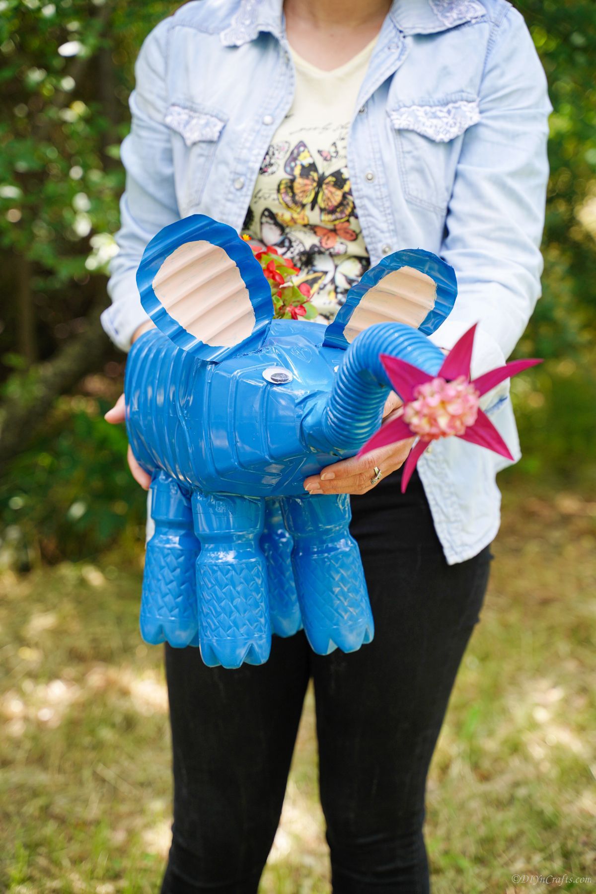 woman in black pants holding bright blue elephant planter