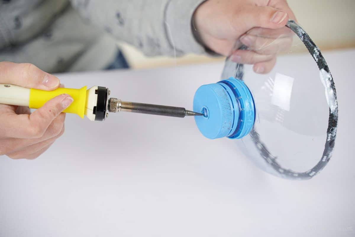 soldering iron being used to make hole in top of blue bottle lid