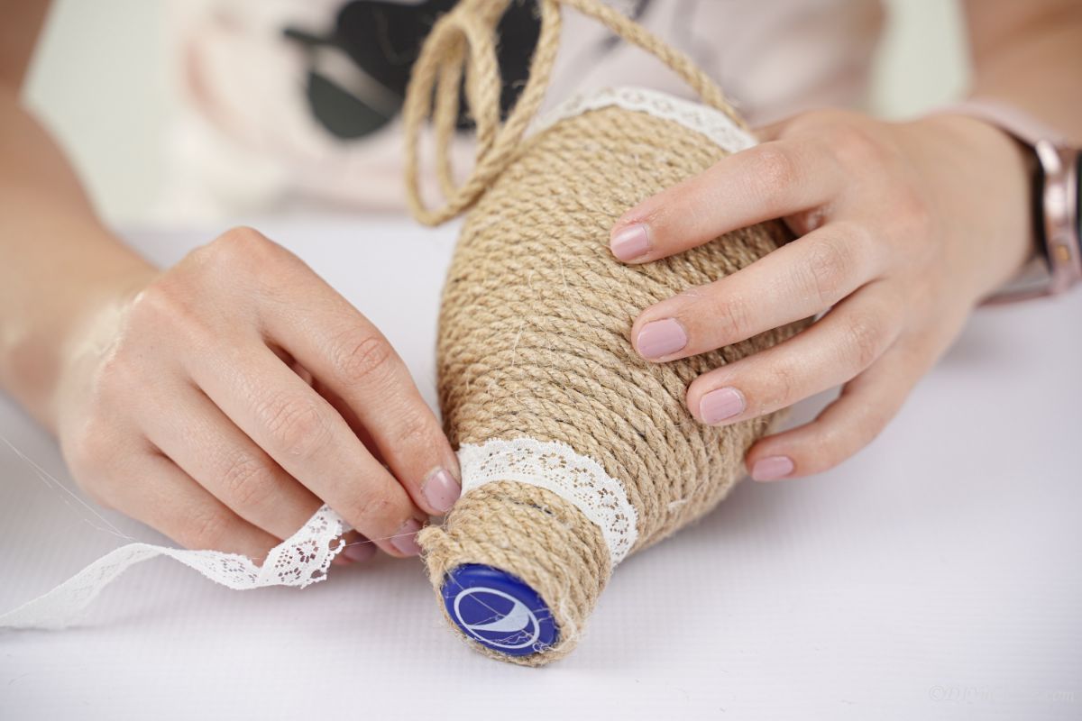 lace ribbon being wrapped around neck of twine wrapped water bottle