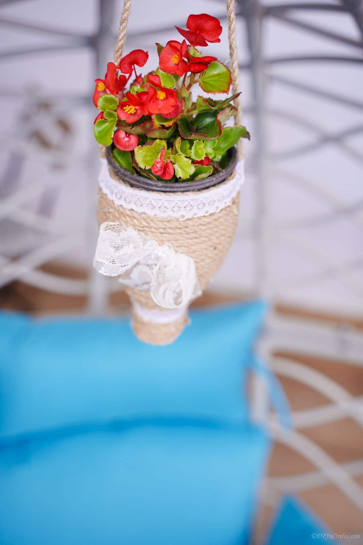 flowers in planter hanging above white wicker chair with blue cushion