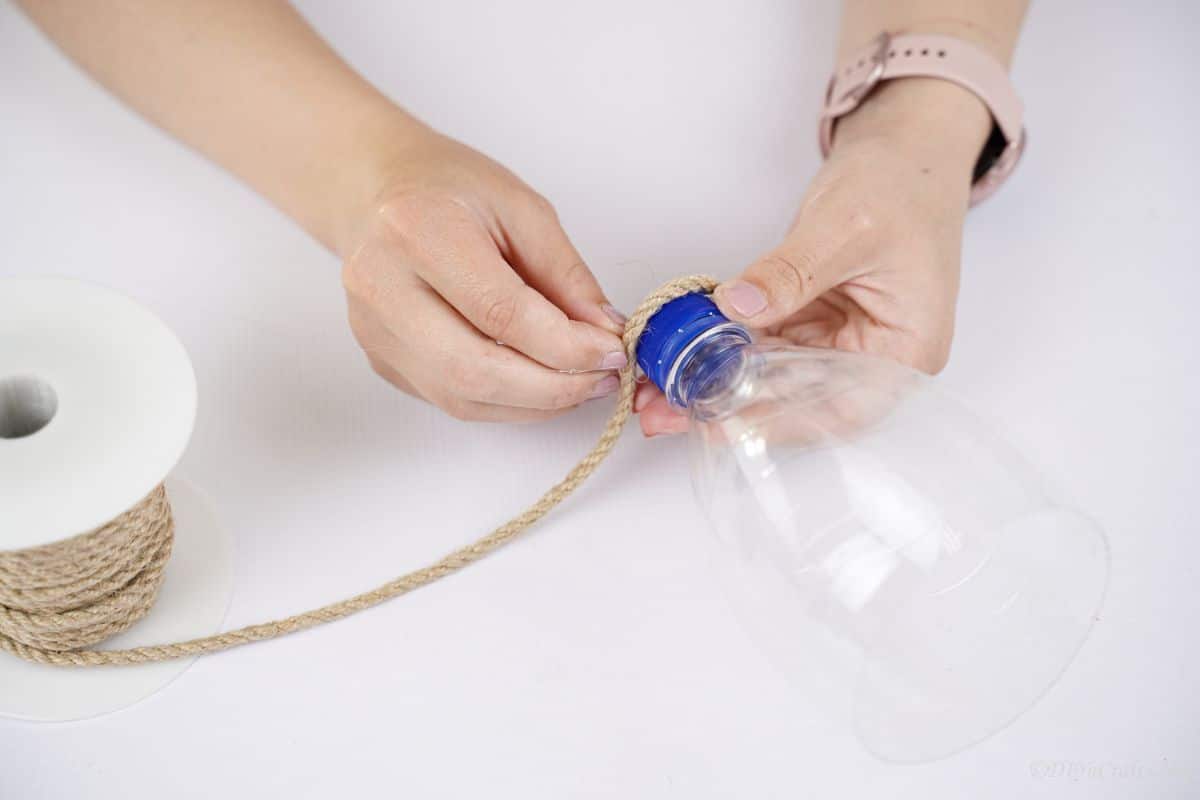 hand wrapping twine around neck of water bottle