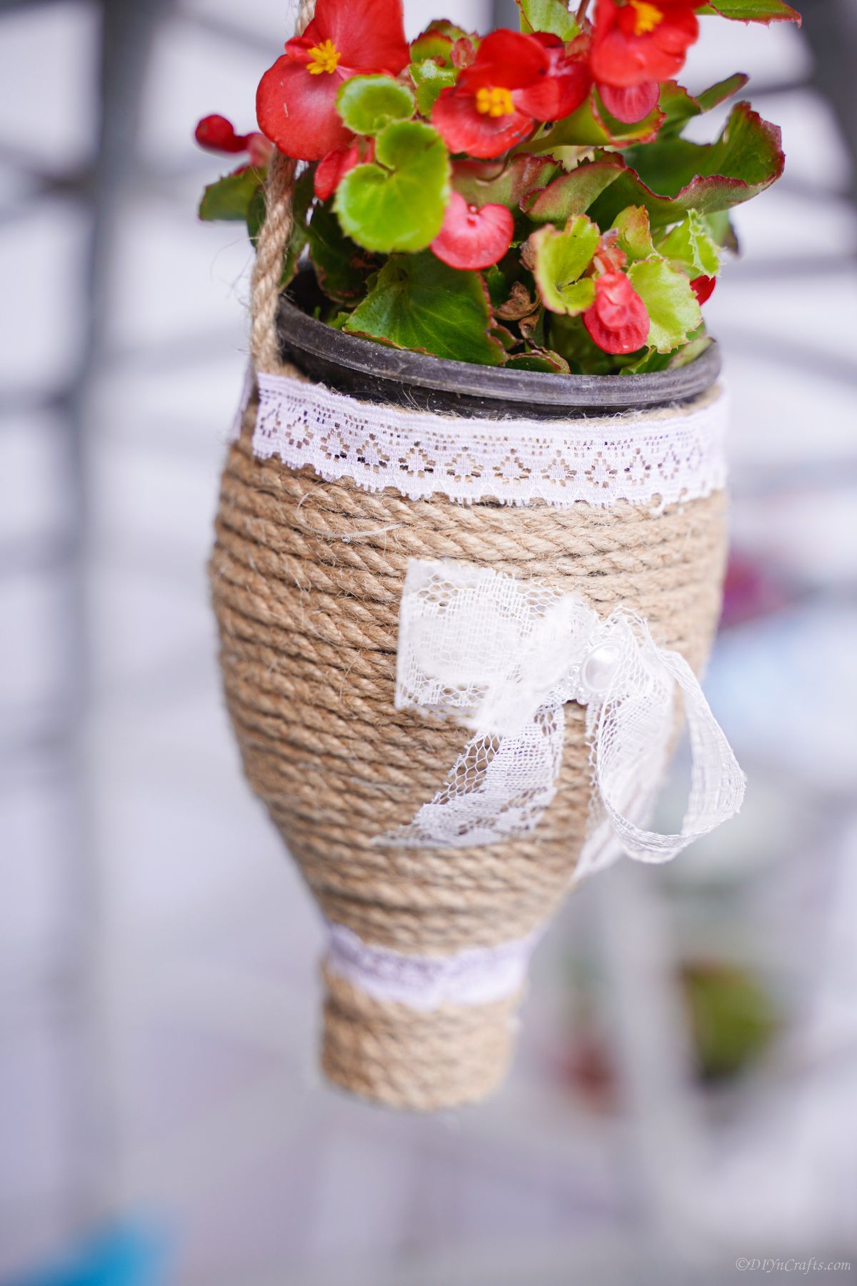 close up photo of twine wrapped bottle planter with red flowers