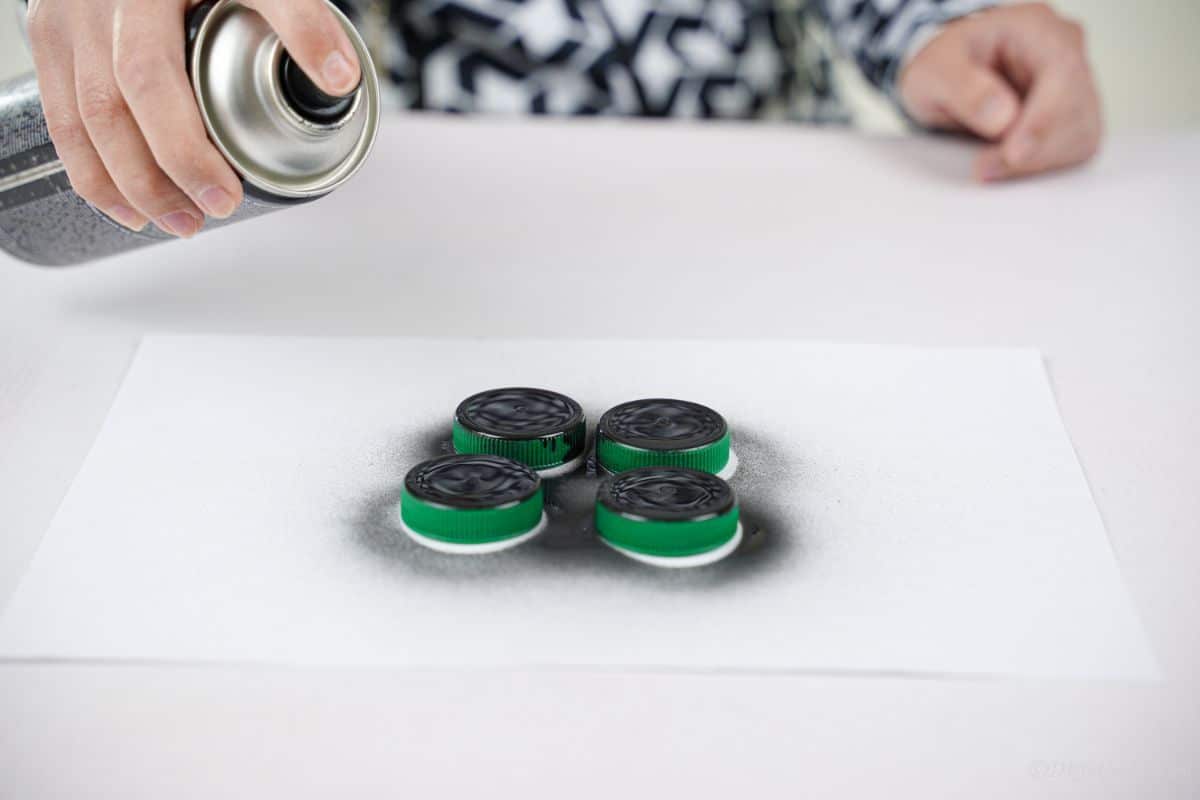 four bottle lids on white paper being painted black