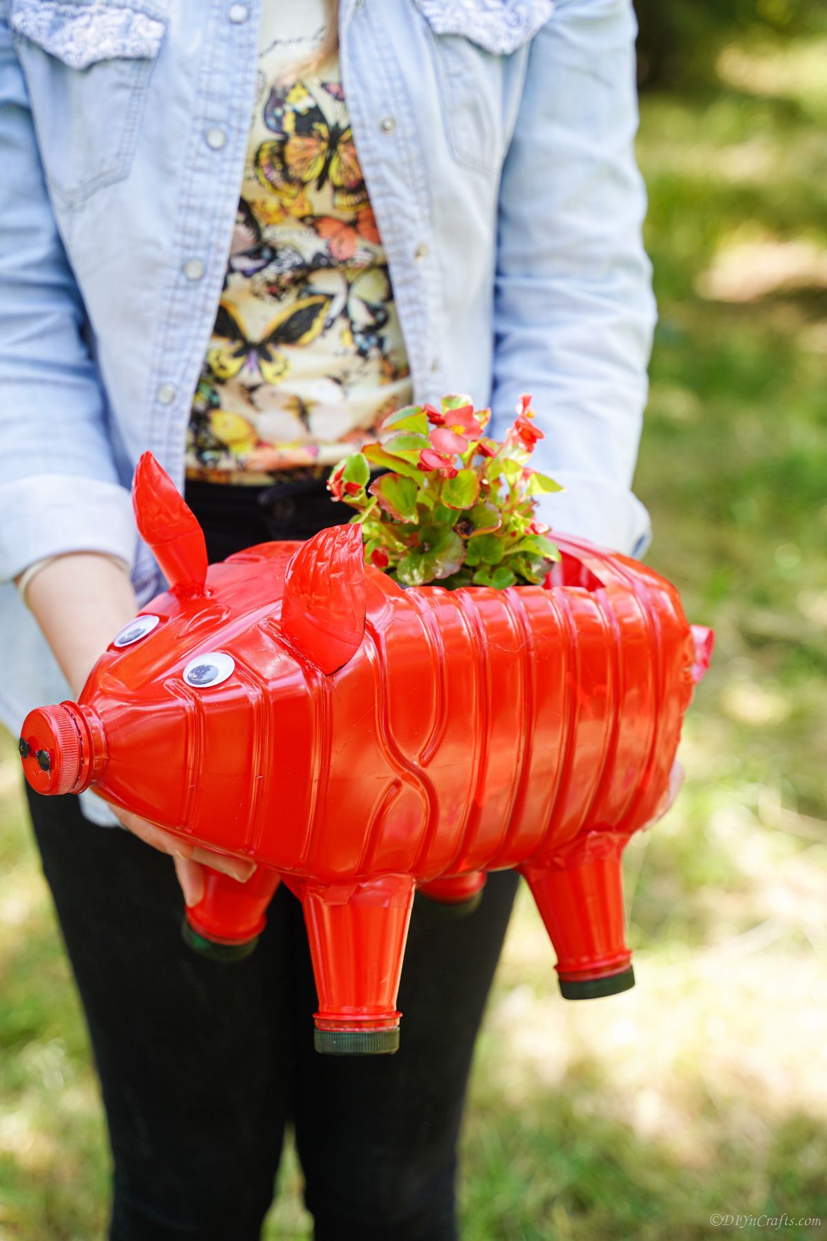lady in blue shirt holding red pig planter with red flowers