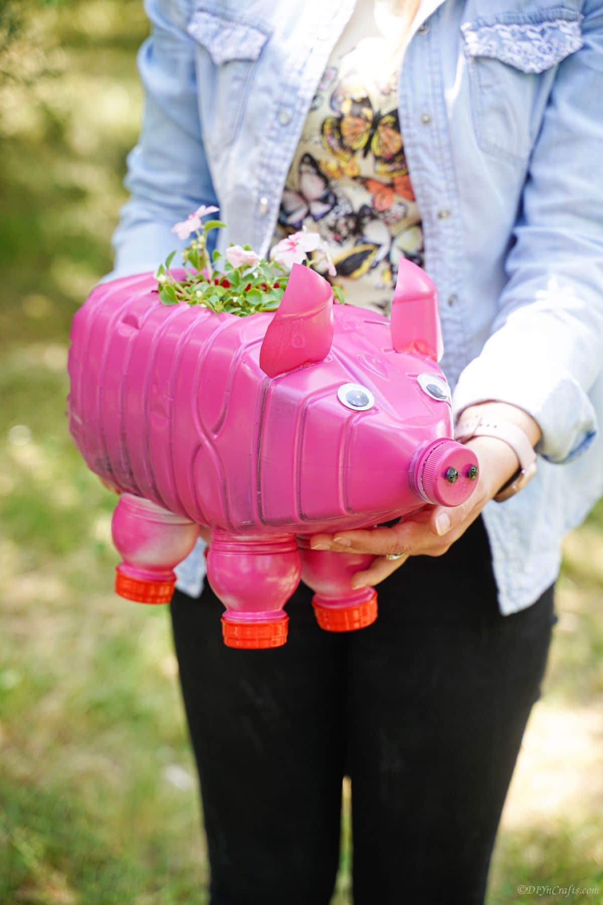 woman holding pink plastic bottle pig planter with whtie flowers