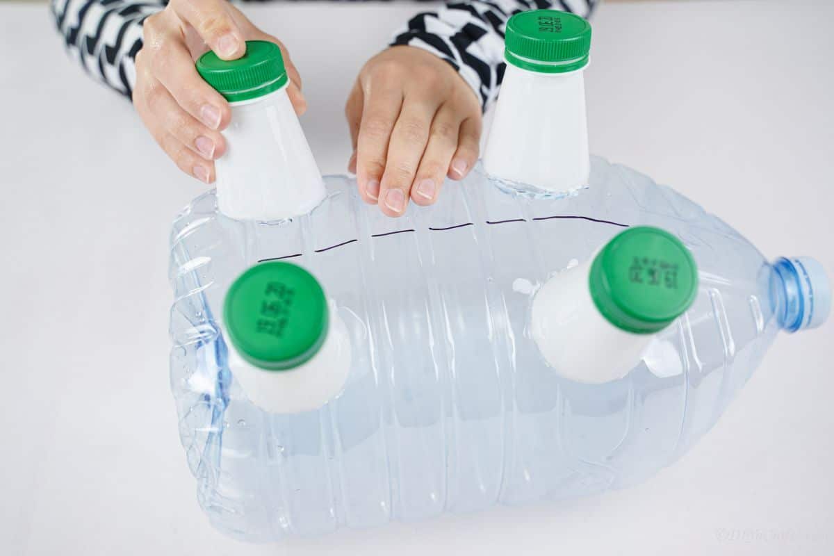 hand holding half bottles onto bottom of gallon bottle to glue onto as feet