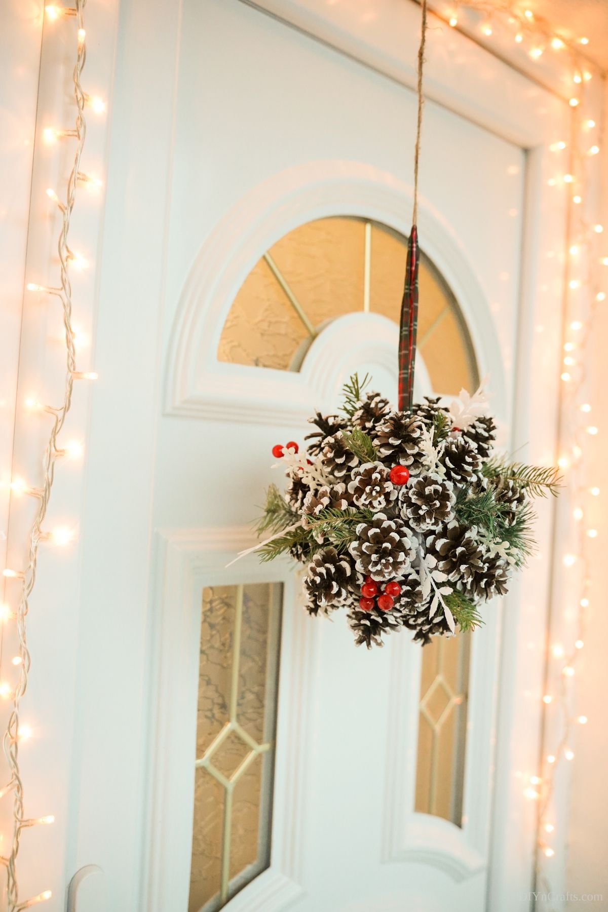 pine cone christmas ball hanging on front door with christmas lights around side of door