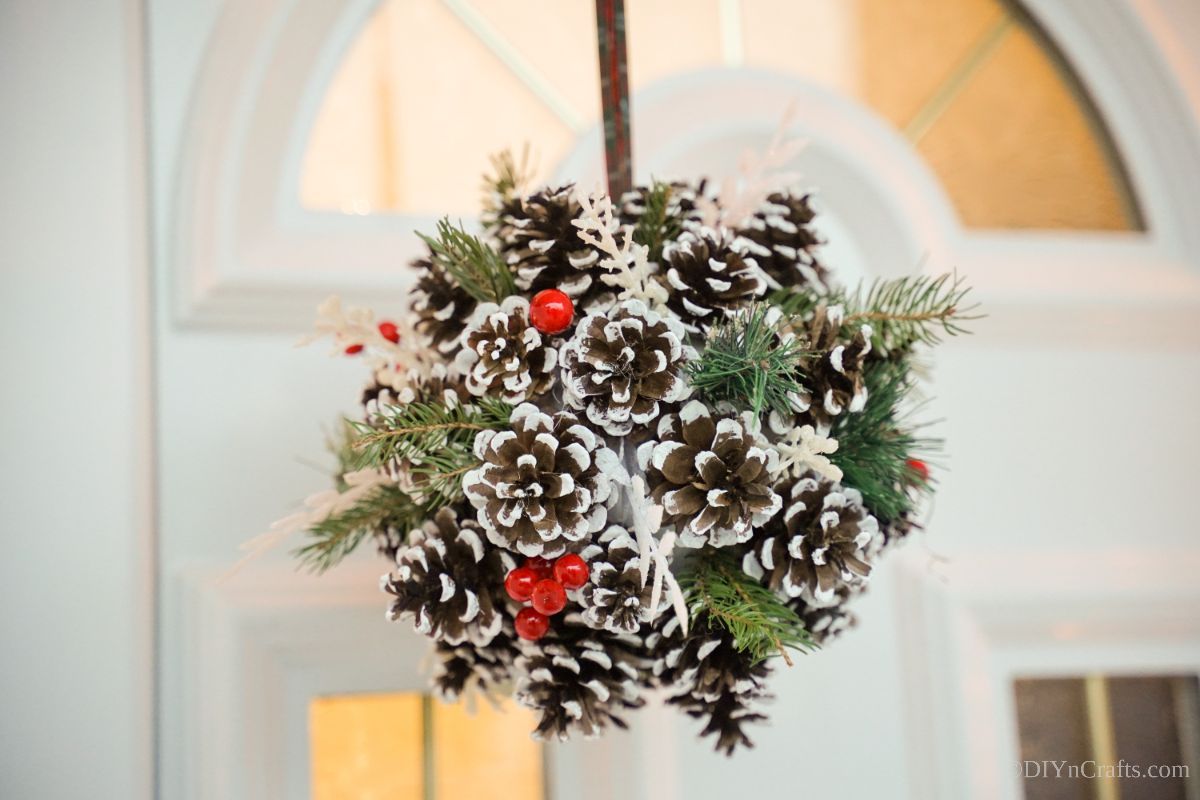 christmas pinecone ball hanging against white door with glass panes
