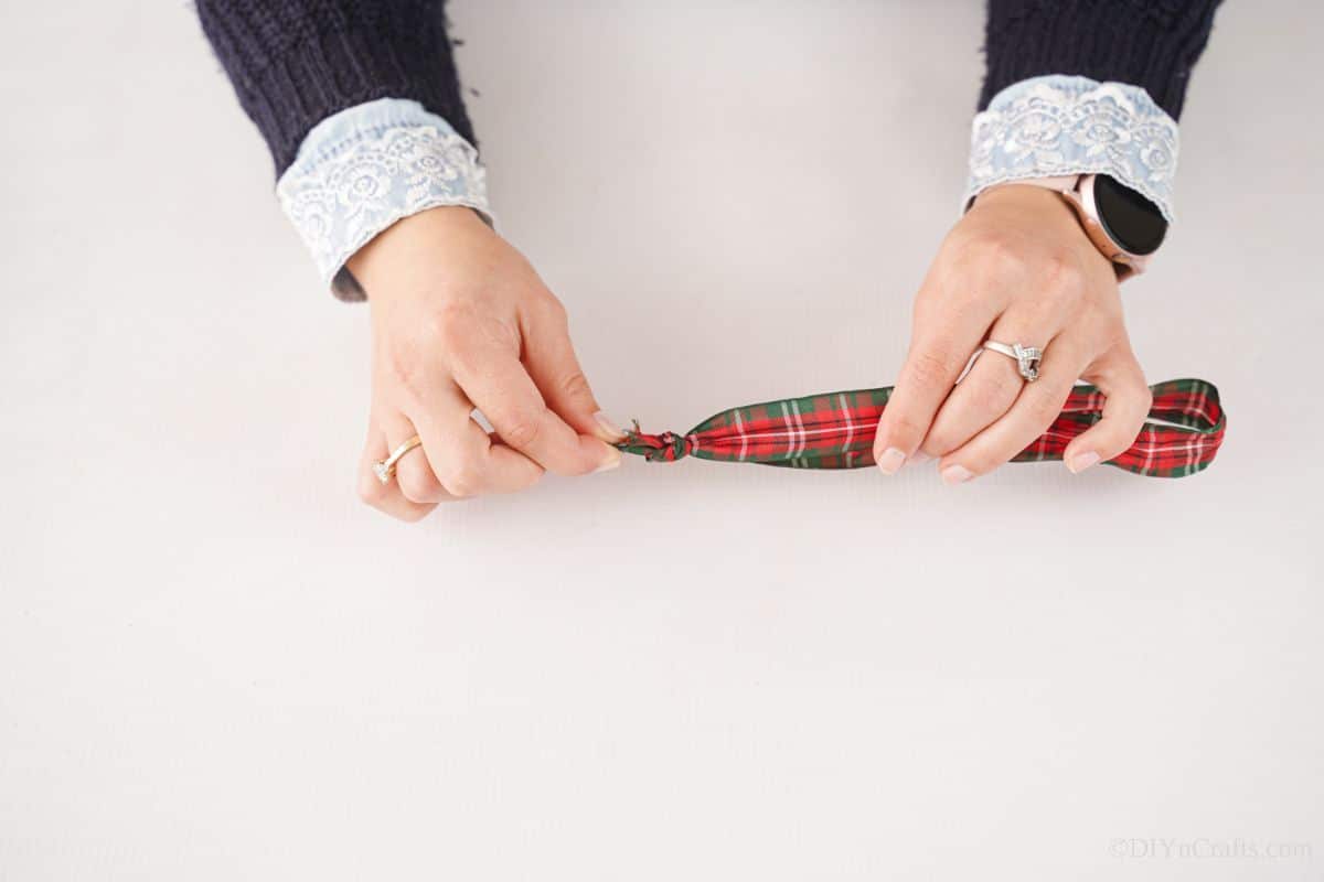 hands tying a length of plaid ribbon into a loop