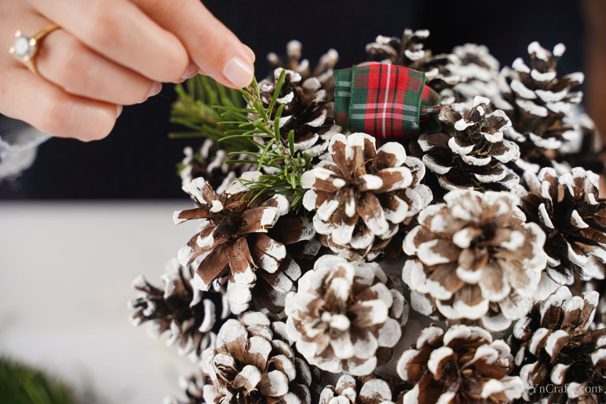 hand adding fake greenery in between pinecones