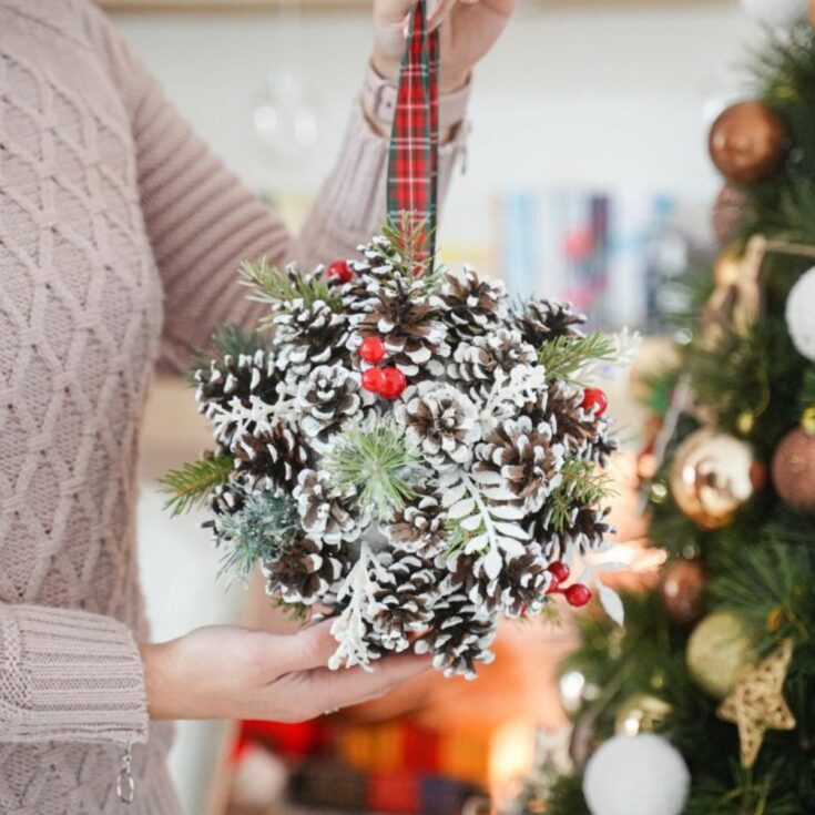 pinecone ball held by woman in front of Christmas tree