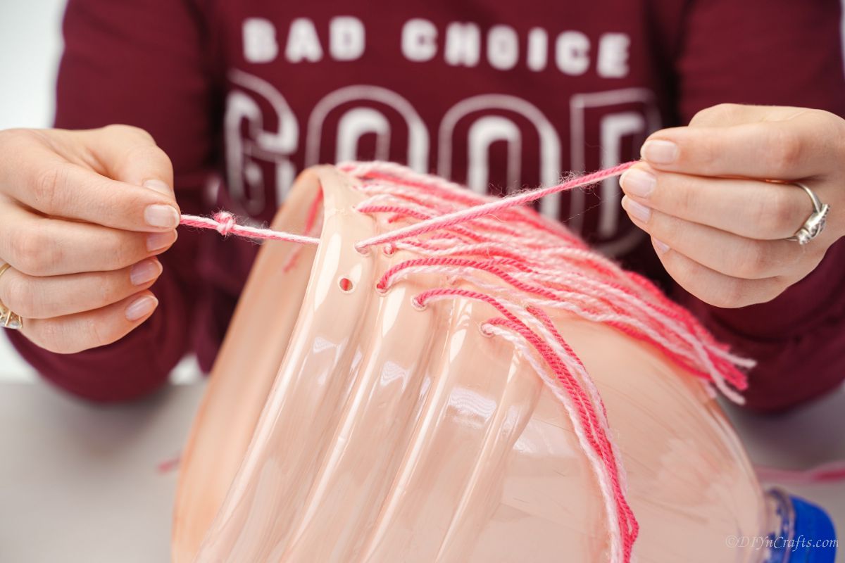 pink yarn being twisted and tied on back of cream bottle