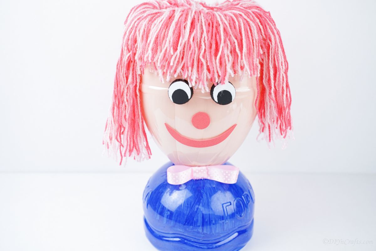 pink yarn hair on bottle doll sitting on white table