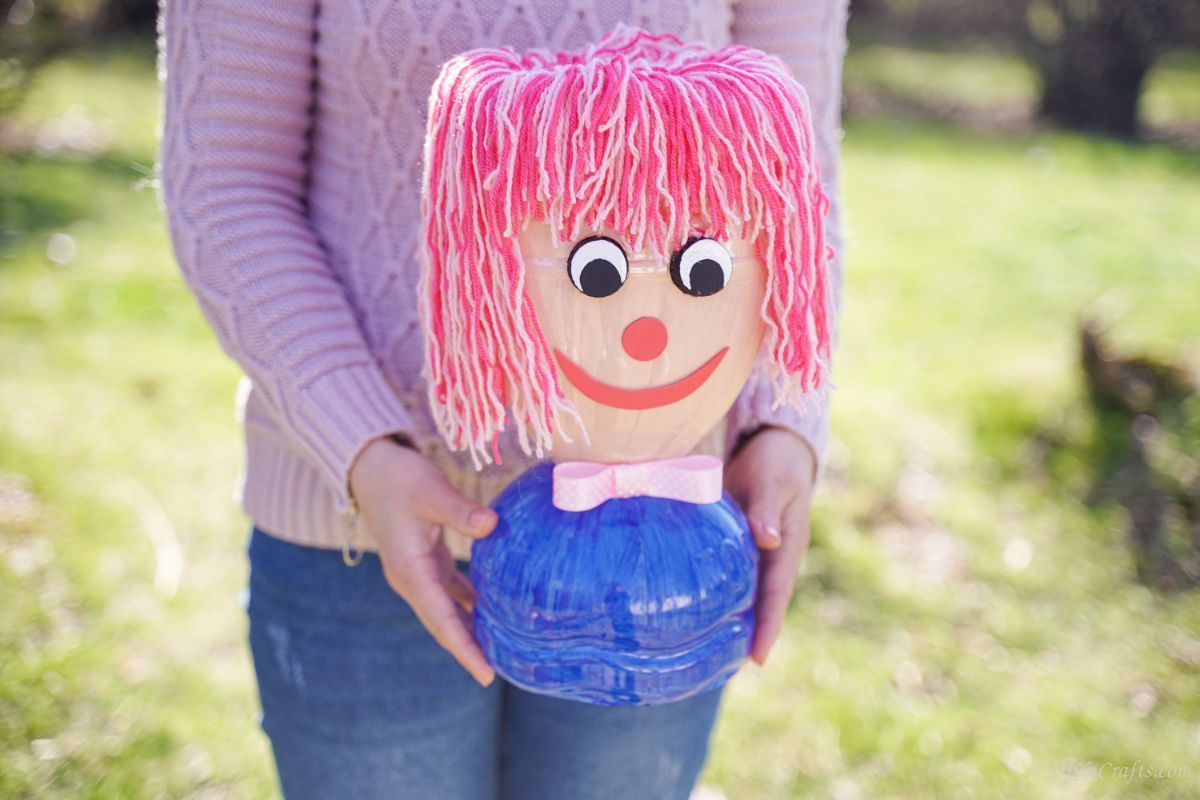 woman in purple holding plastic bottle doll head