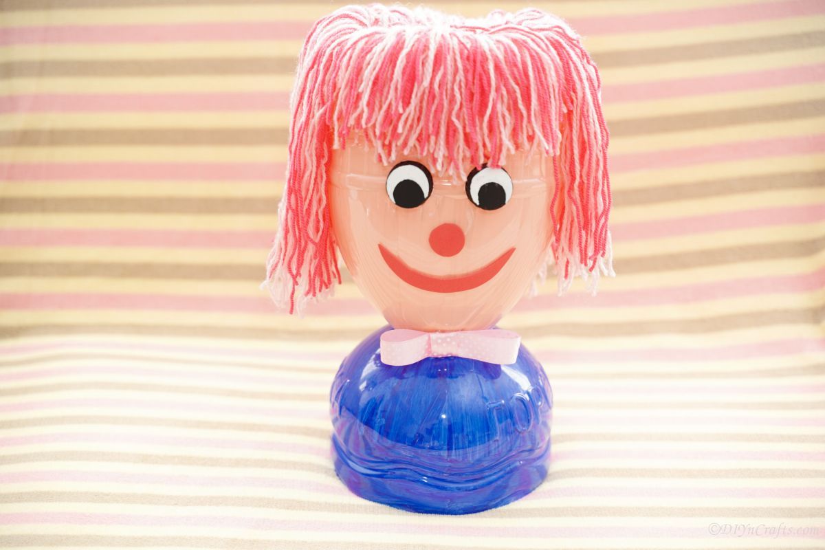 plastic bottle doll head on table with striped background