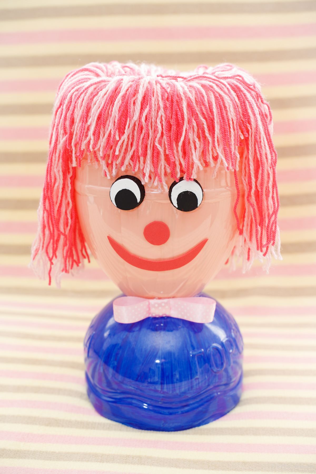 striped background behind bottle doll with pink yarn hair