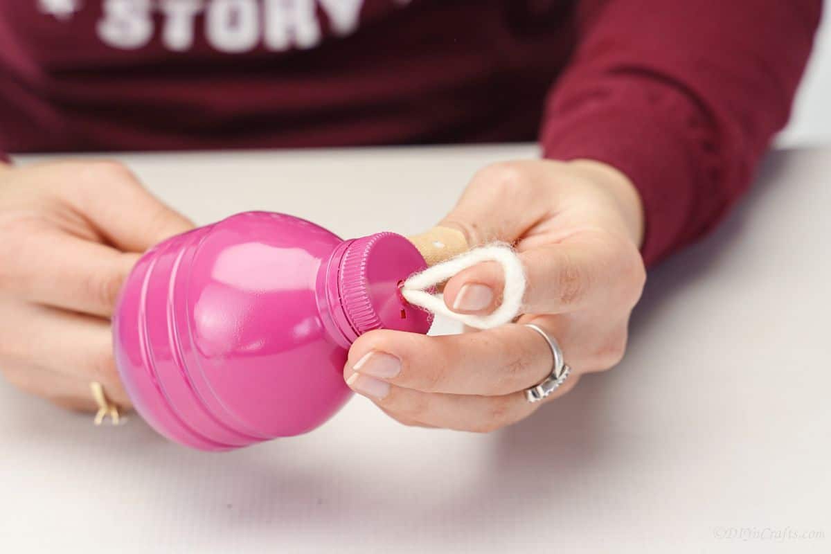 rope loop being pushed through top of pink bottle lid
