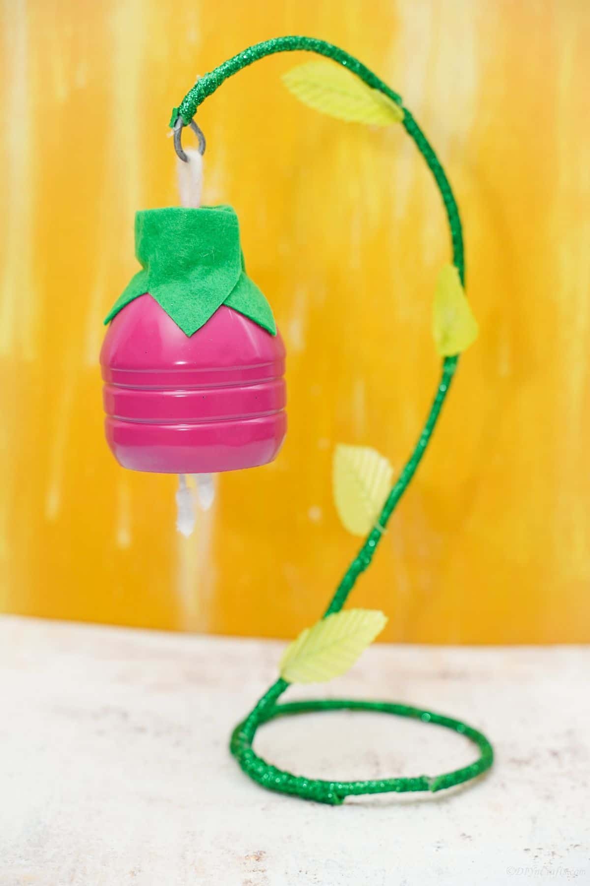 pink hanging plastic bottle flower on green wire stem with yellow background