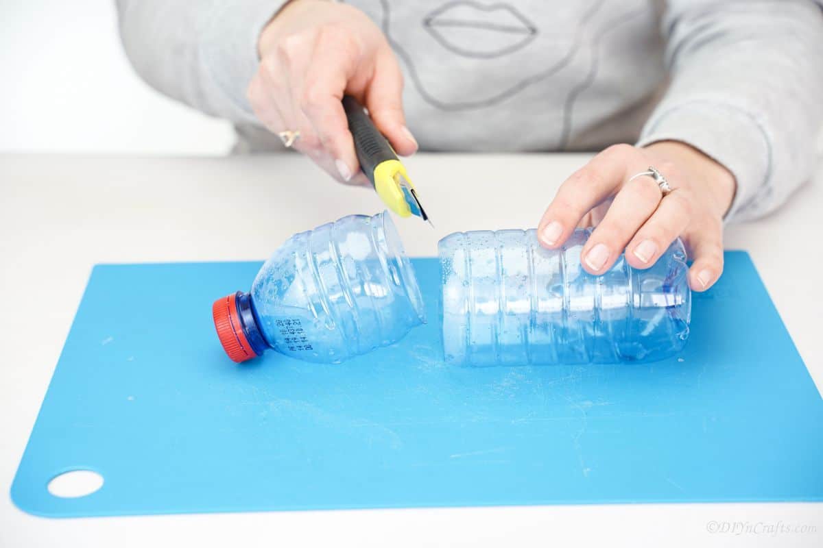 craft knife cutting plastic bottle on blue mat