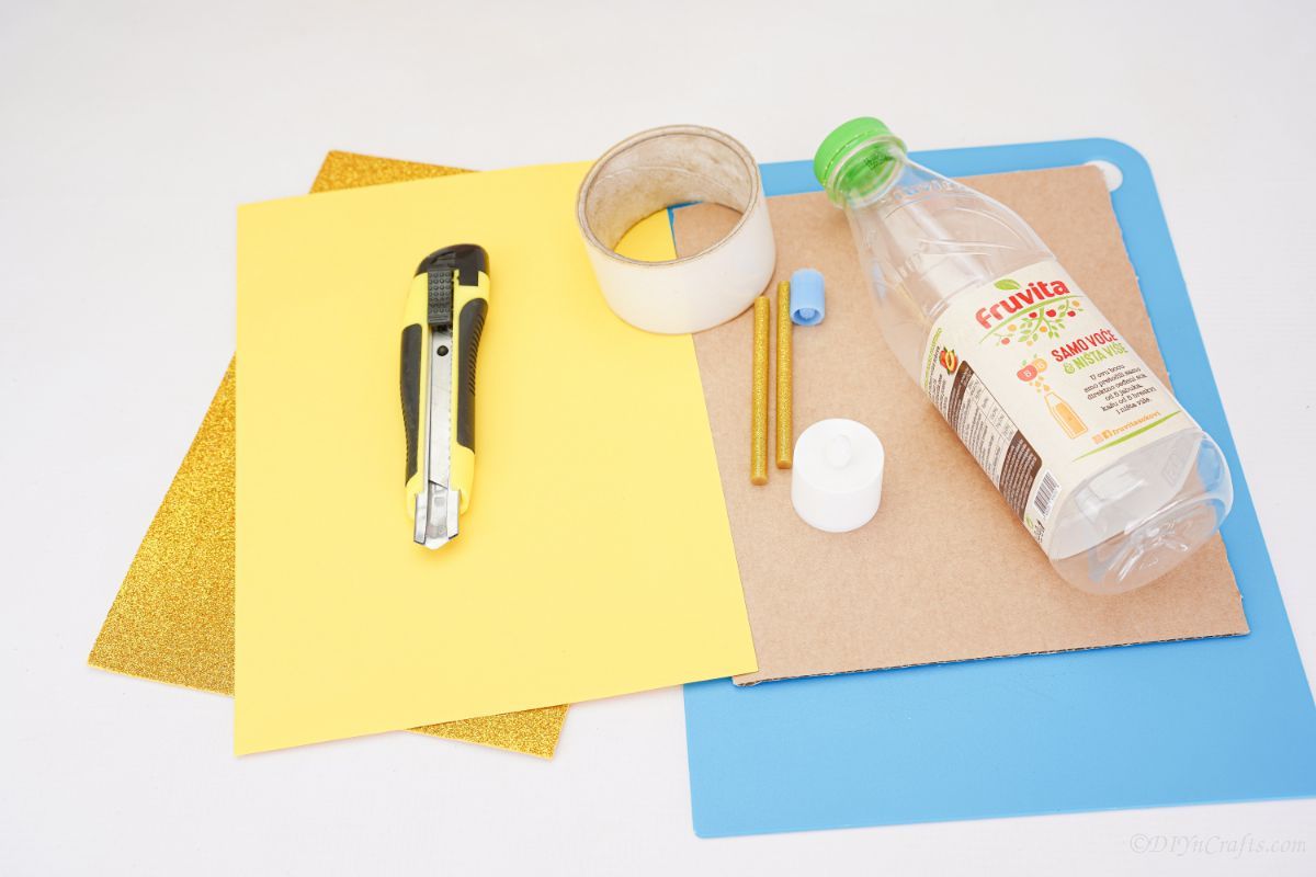 craft knife yellow nga papel ug karton sa lamesa nga adunay botelya