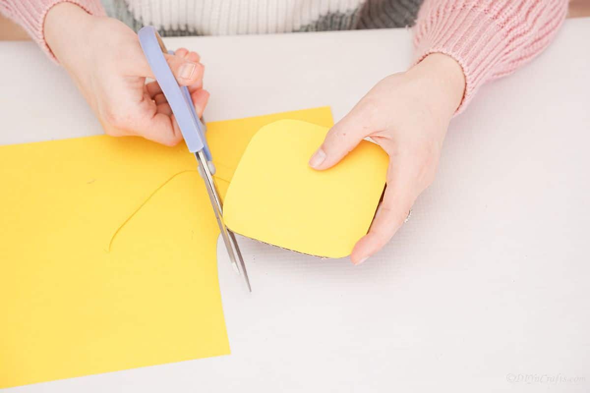 blue scissors trimming yellow paper into rounded square