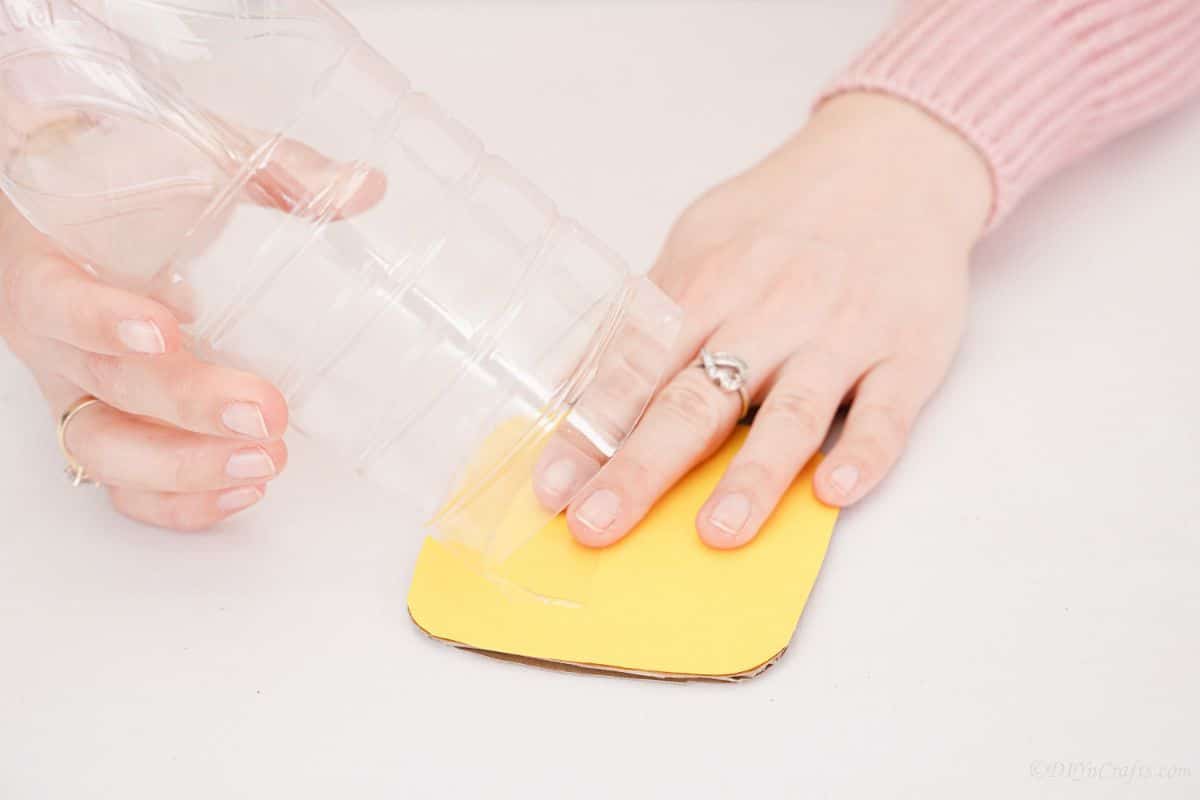 hand holding yellow cardboard square below plastic bottle