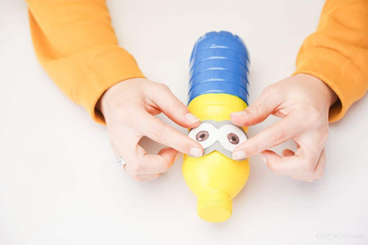 hand gluing goggles onto minion bottle