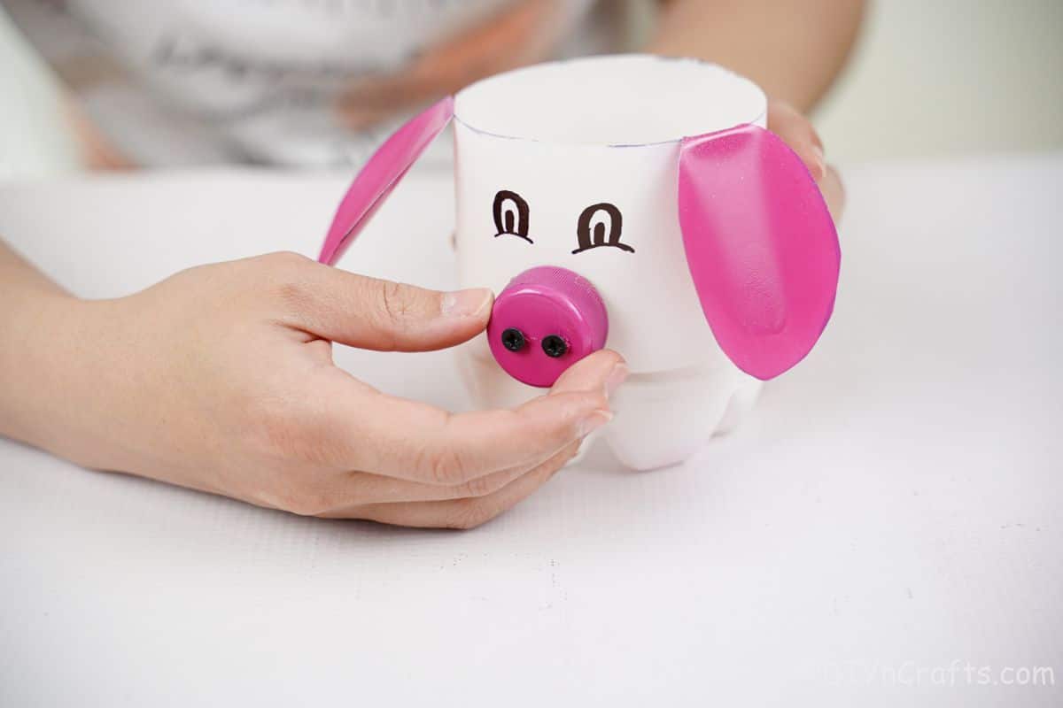 hand putting pink bottle cap pig nose on front of white bottle planter
