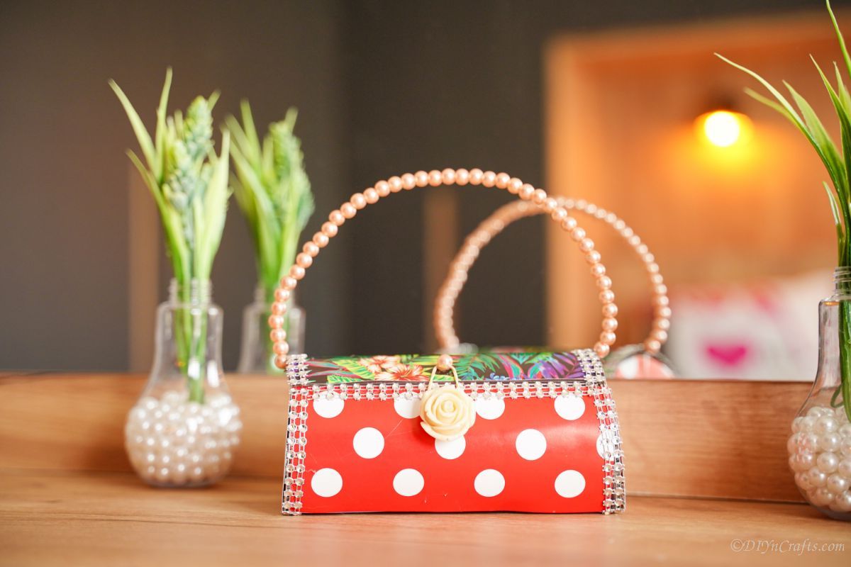 small red and white purse with pearl handle on table by potted plant