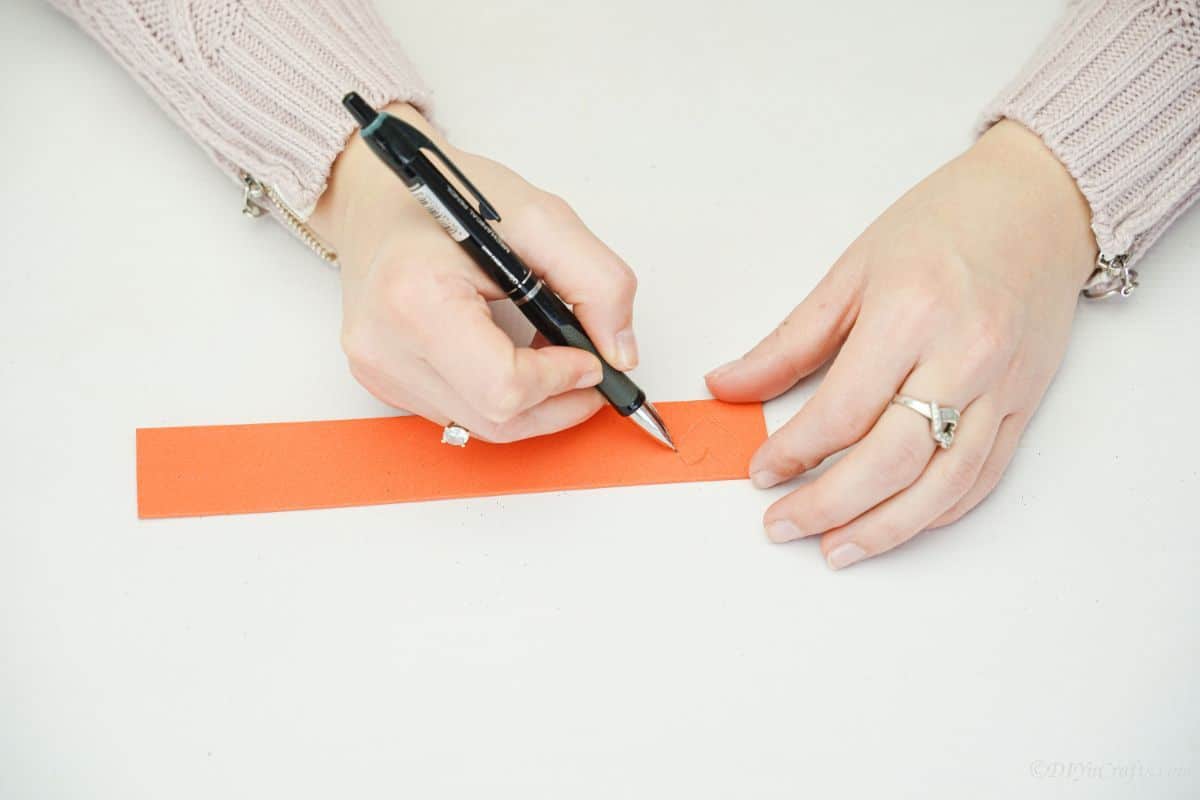 hand using black pen to draw on orange foam paper